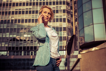 Fototapeta premium Beautiful business woman talking on a cell phone in front of the office building