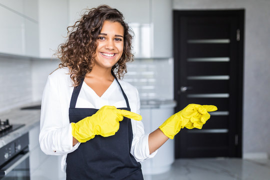 Pretty young latin cleaning lady pointing fingers at blank white board with kitchen in background