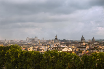 Fototapeta na wymiar Roofs of Rome with cupolas of ancient churches and altare della Patria in the distance. Shot on a rainy day with stormy clouds and mist