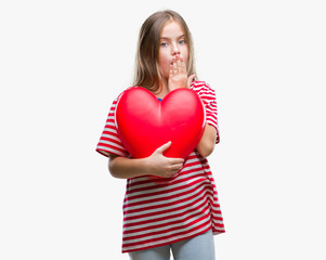 Fototapeta na wymiar Young beautiful girl holding red heart over isolated background cover mouth with hand shocked with shame for mistake, expression of fear, scared in silence, secret concept