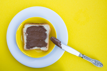 One slice of toast bread with chocolate cream in  the colorful plates on the yellow  background.Top view.Copy space.