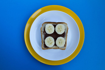 One slice of toast bread with chocolate cream and banana in the colorful plates on the blue...