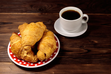 Cup of coffee and plate with fresh croissants on wooden table