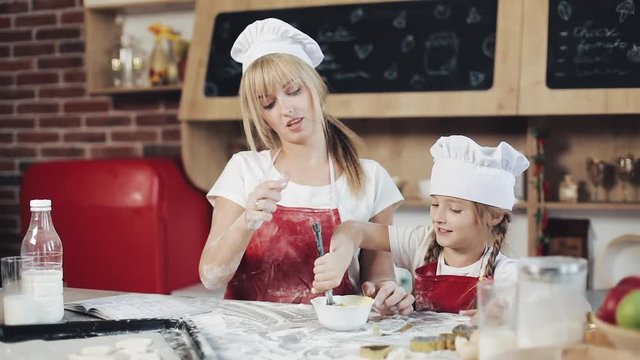 Mom and daughter in the same clothes have fun preparing a dough on a cozy kitchen. They mixing eggs in bowl at the kitchenl. Cooking, Mom and daughter concept