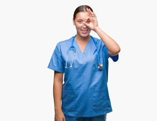 Young caucasian doctor woman wearing medical uniform over isolated background doing ok gesture with hand smiling, eye looking through fingers with happy face.
