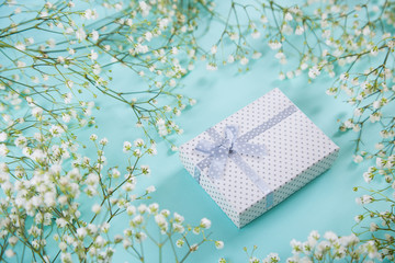Gift box surrounded with white gypsophila flowers on mint blue background, high angle.