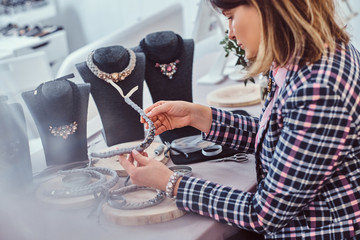 Elegantly dressed woman makes handmade necklaces, working with needles and thread in workshop.