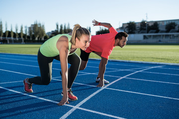 Athlete couple at starting position ready to start a race. Sprinters ready for race on race track. Woman against man.