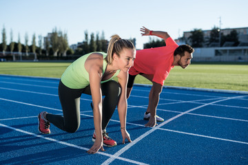 Athlete couple at starting position ready to start a race. Sprinters ready for race on race track. Woman against man.