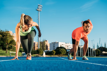 Athlete couple at starting position ready to start a race. Sprinters ready for race on race track....