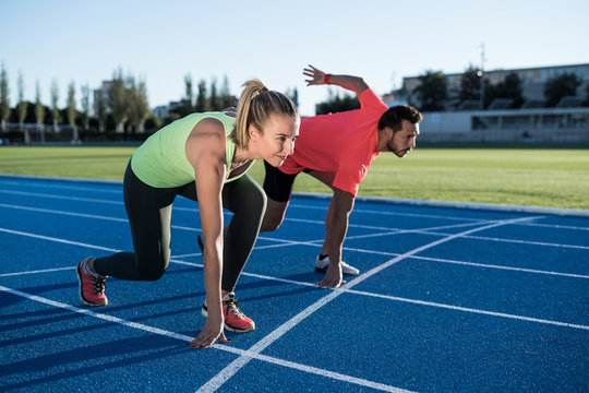 Athlete couple at starting position ready to start a race. Sprinters ready for race on race track. Woman against man.