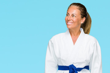 Middle age adult woman wearing karate kimono uniform over isolated background looking away to side with smile on face, natural expression. Laughing confident. © Krakenimages.com