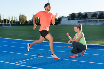 Obraz premium Woman is timing to runner with chronometer at the end of run in a race track. Competition.