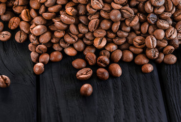 Roasted fragrant beans of black coffee are scattered on a black table