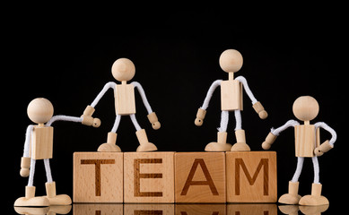 Teamwork concept, Wood cube block with word “TEAM” and Wooden Stick Figures team. black background, reflecting.