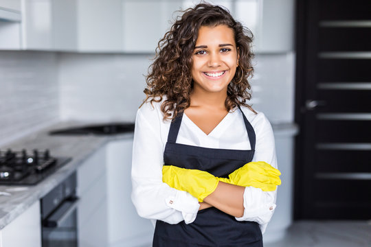 Young american smiling woman wearing apron and rubber gloves, standing in kitchen