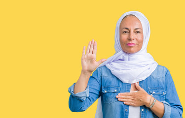 Middle age eastern arab woman wearing arabian hijab over isolated background Swearing with hand on chest and open palm, making a loyalty promise oath