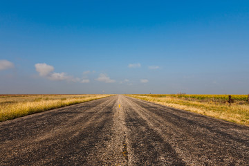 Fototapeta na wymiar Old black worn country road against blue sky in rural Texas, USA