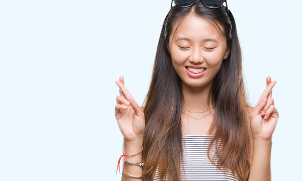 Young asian woman wearing sunglasses over isolated background smiling crossing fingers with hope and eyes closed. Luck and superstitious concept.