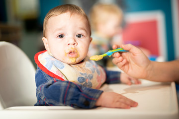 A baby child eats food with mother spoon