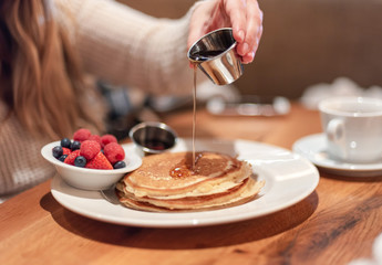 Closeup of young woman pouring warm syrup on pancakes