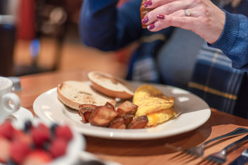 Meeting a friend for breakfast, woman adding pepper to her omlette