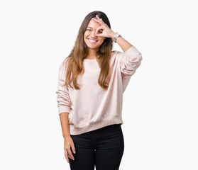 Obraz na płótnie Canvas Young beautiful brunette woman wearing pink sweatshirt over isolated background doing ok gesture with hand smiling, eye looking through fingers with happy face.