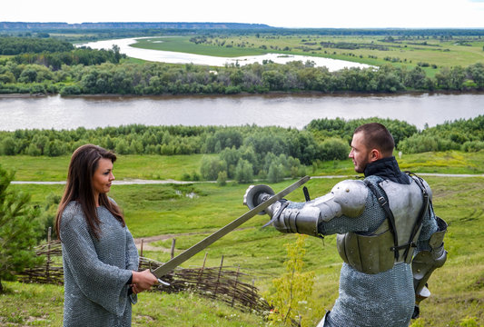 A lady in chain mail and a knight in armor learn to hold a weapon and defend themselves from the blows of a sword. Knightly armor and weapon. Semi - antique photo.