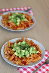 Two plates of pasta with tomato sauce, peppers, corn, avocado and herbs. Selective focus.