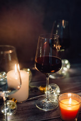 Holidays composition made of glass of red wine, candles and garlands on a dark background