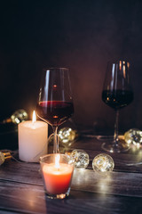Holidays composition made of glass of red wine, candles and garlands on a dark background