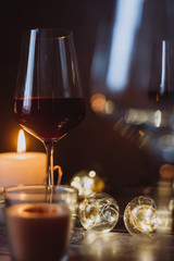 Holidays composition made of glass of red wine, candles and garlands on a dark background
