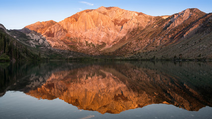 Fototapeta na wymiar Panorama of the golden light of sunrise on mountain peaks reflected in the calm waters of Convict Lake in the eastern Sierra Nevada mountains of California