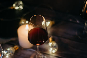 Holidays composition made of glass of red wine, candles and garlands on a dark background