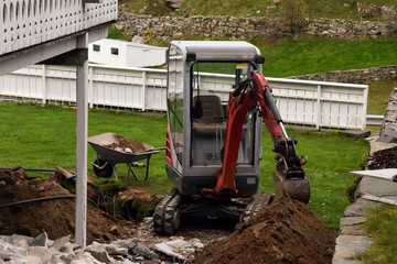 Small excavator without a driver in the cabin. Next is a broken road tile.