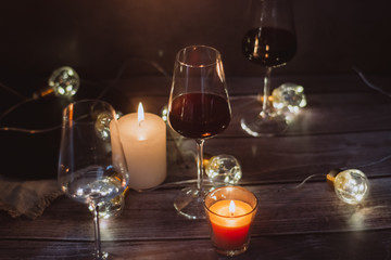 Holidays composition made of glass of red wine, candles and garlands on a dark background