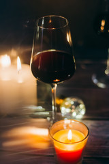Holidays composition made of glass of red wine, candles and garlands on a dark background