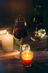 Holidays composition made of glass of red wine, candles and garlands on a dark background