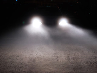 Car driving in dense fog trough the yard with bright headlamps. Dangerous road conditions. Night...
