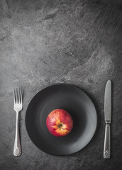 Red apple on black plate with knife and fork. Dark background. Overhead shot with copy space.