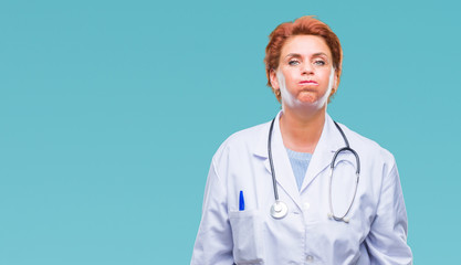 Senior caucasian doctor woman wearing medical uniform over isolated background puffing cheeks with funny face. Mouth inflated with air, crazy expression.