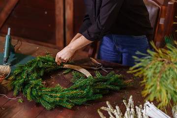 Young Cute smiling Woman designer preparing Christmas Evergreen Tree Wreath. Manufacturer of Christmas decor with their own hands. Christmas wreath for the holiday. The new year celebration. Closeup