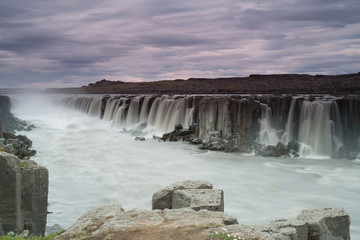 The Sellfoss Waterfall with golden clouds in the sky. The flowing water is captured by a long exposure. Amazing blue color of water from the glacier. Natural and colorful environment. Iceland..