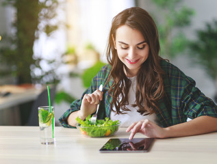 healthy eating. happy young girl eating salad with tablet pc in  morning in kitchen.