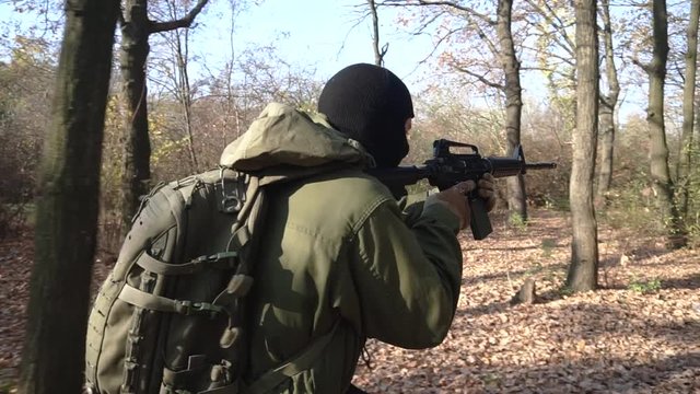 Soldier in green uniform and black mask  with assault rifle walking in the autumn forest 