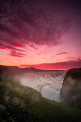 The Gullfoss Waterfall with golden clouds in the sky. The flowing water is captured by a long...