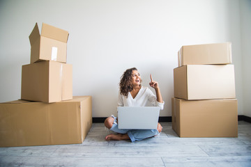 Young latin american woman moving in a new flat, sitting on the floor and surfing the web on a tablet computer and have new decorating ideas.