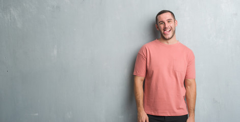 Obraz premium Young caucasian man over grey grunge wall sticking tongue out happy with funny expression. Emotion concept.