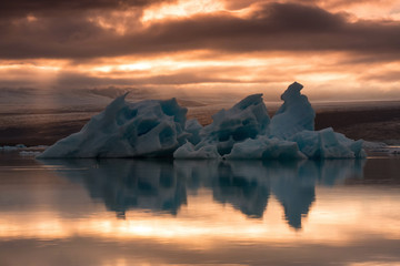 The Jökulsárlón is a large glacial lake in southeast Iceland, the floating ice floes on a quiet surface of gracial lagoon, a dramatic sunset sky is reflected on the surface