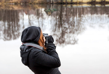girl taking pictures on camera during a trip to the lake cold late autumn reflection of trees, sky, forest